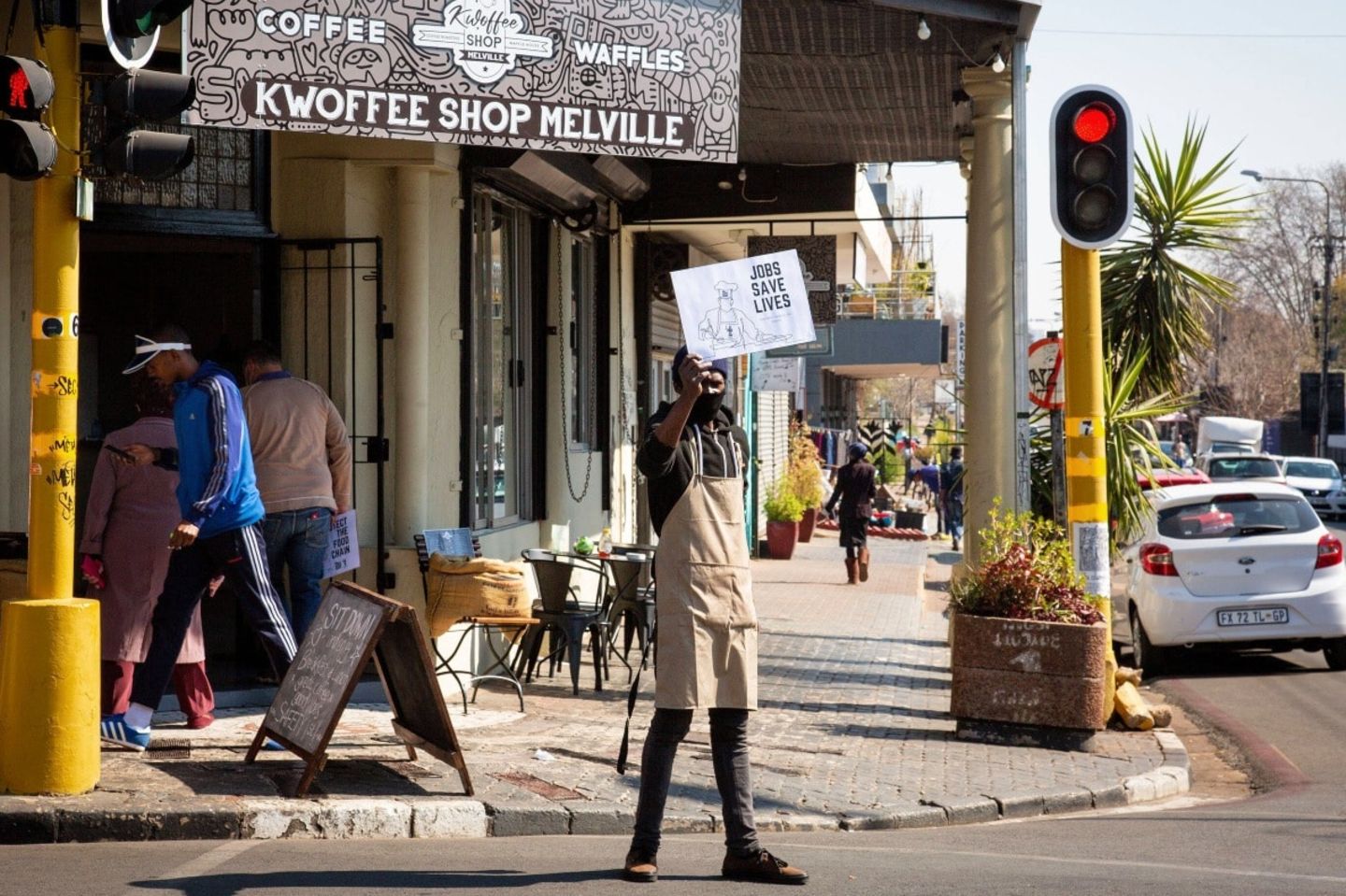 Ein Mann hält eine Schrifttafel mit der Aufschrift "Jobs save lives" vor einem Restaurant in Johannesburg