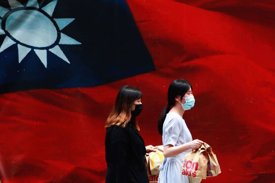 Taiwan: Zwei Frauen mit Gesichtsmasken gehen an einer Landesflagge vorbei