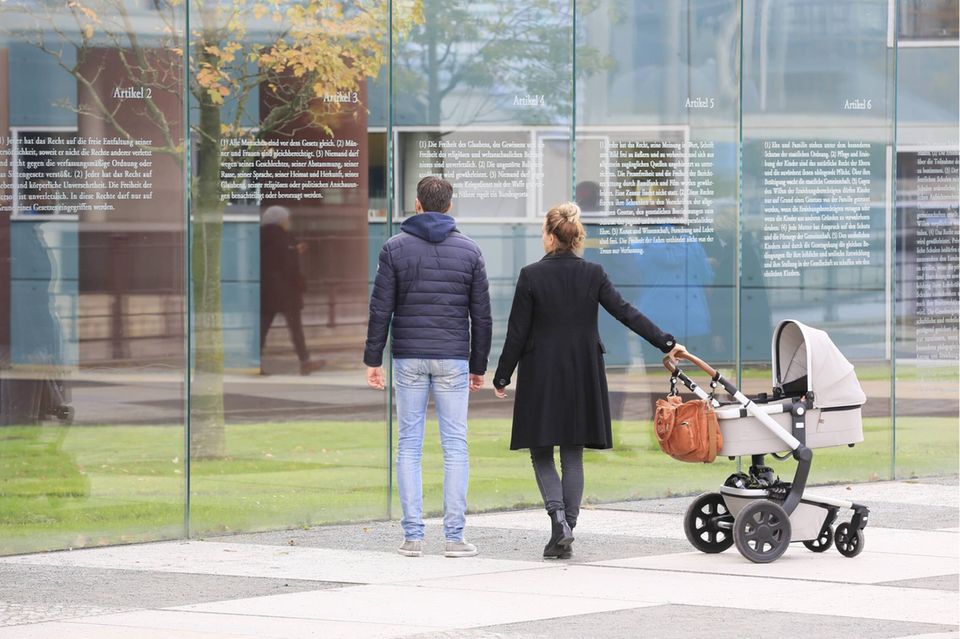 Ein Paar mit Kinderwagen vor der Glaswand mit eingravierten Artikeln des Grundgesetzes am Berliner Reichstagsufer