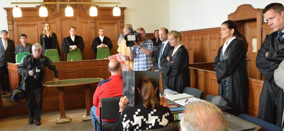 Die Hauptangeklagten Gerald Saik (in rot) und seine Frau verstecken ihre Gesichter beim Prozessauftakt