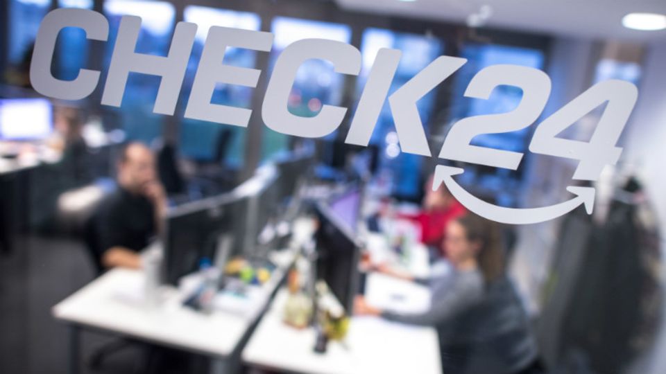 Mitarbeiter sitzen in der Zentrale des Vergleichsportals Check24 in München an ihren Schreibtischen hinter einer Glasscheibe, auf der das Logo des Unternehmens zu sehen ist.