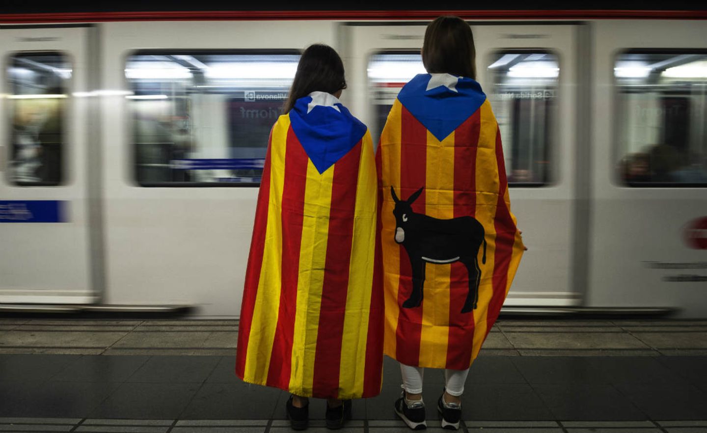 Zwei in katalanische Flaggen gehüllte Mädchen stehen an einer U-Bahn-Station