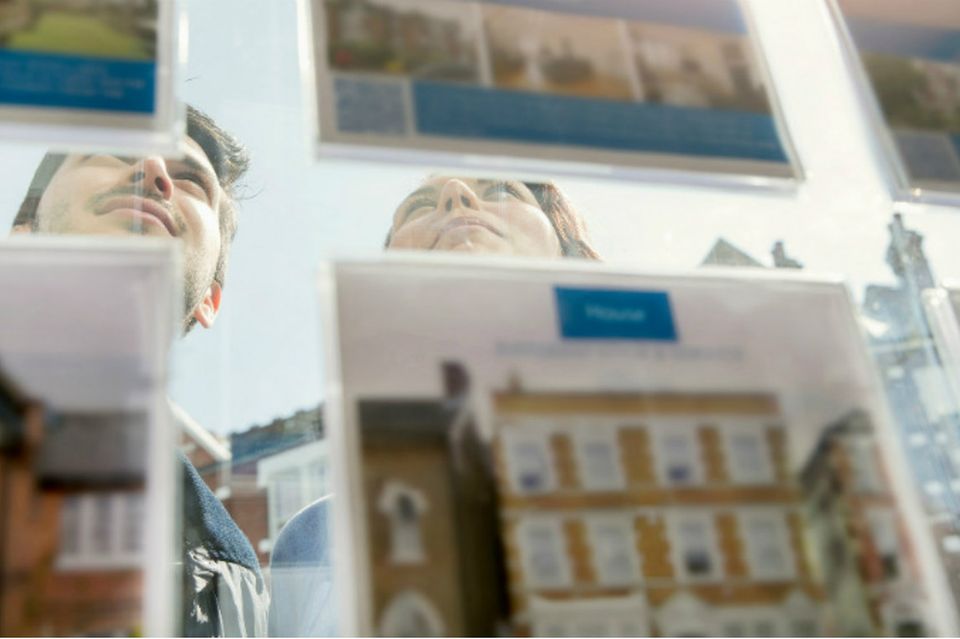 Ein junges Paar studiert Immobilienanzeigen in einem Schaufenster