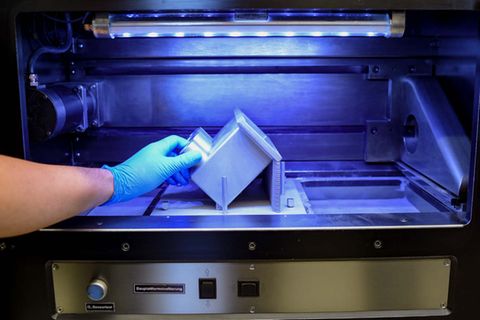 Ein Techniker entnimmt einem 3-D-Drucker ein fertig gedrucktes Bauteil eines ICE. Die Bahn setzt die 3-D-Drucktechnologie verstärkt bei Instandhaltungsarbeiten ein.