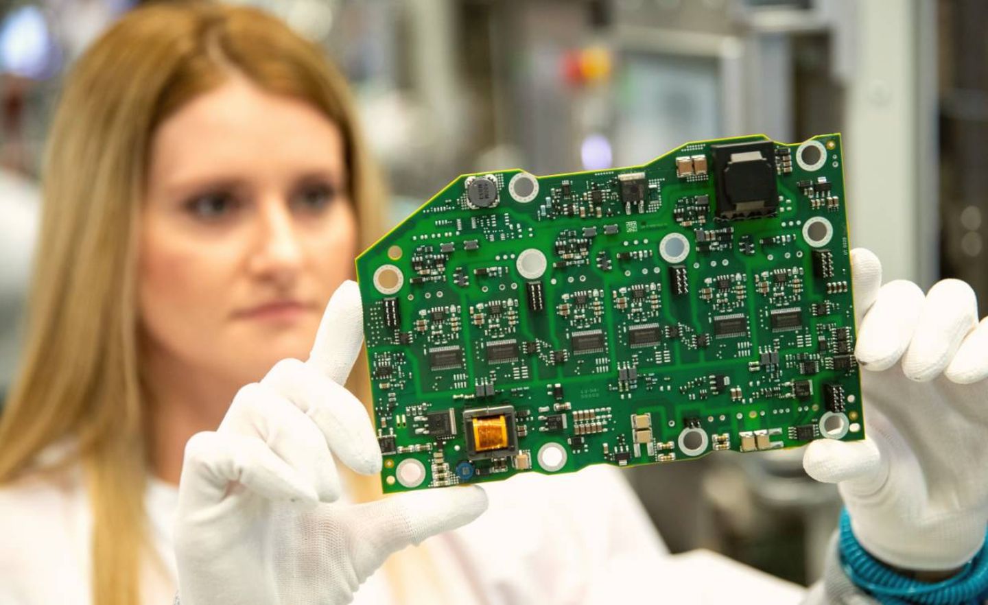 Eine Mitarbeiterin bei Continental hält in der Produktion der Leistungselektronik für Elektrofahrzeuge eine Leiterplatte mit der Steuerungs-Elektronik in der Hand.