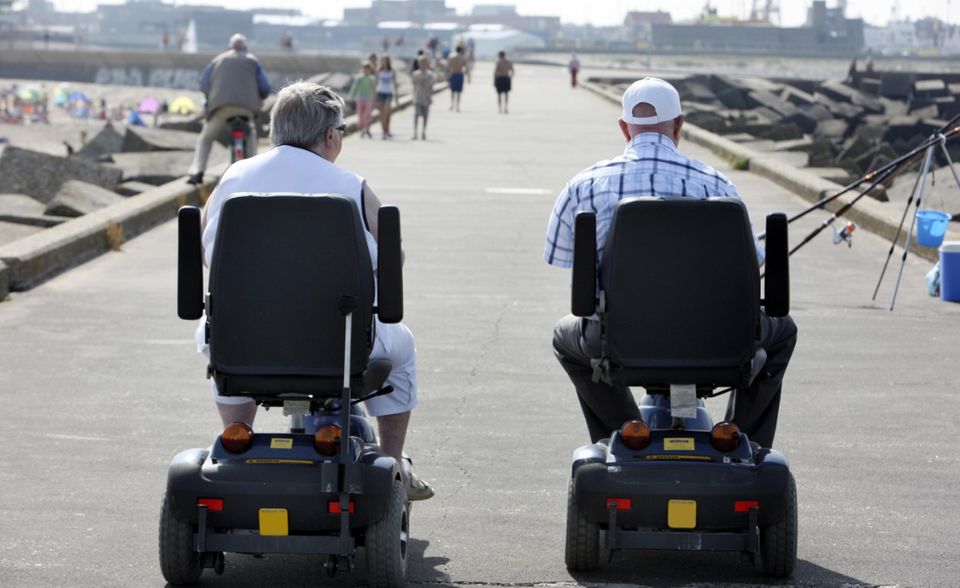 Senioren auf motorisierten Rollstühlen auf einem betonierten Wellenbrecher am Strand von Scheveningen