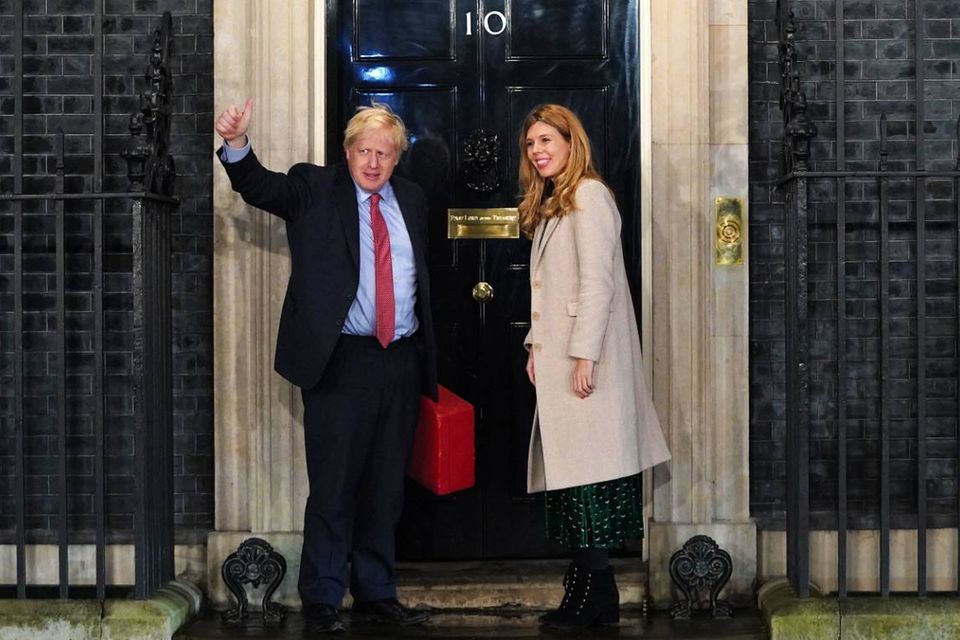 Boris Johnson winkt vor der Tür des Regierungssitzes in der Downing Street. Neben ihm steht seine Partnerin Carrie Symonds
