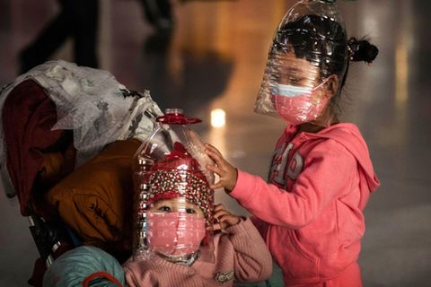 Mit Mundschutz und Plastikflaschen über dem Kopf wollen sich chinesische Kinder vor einer Ansteckung mit dem Coronavirus schützen