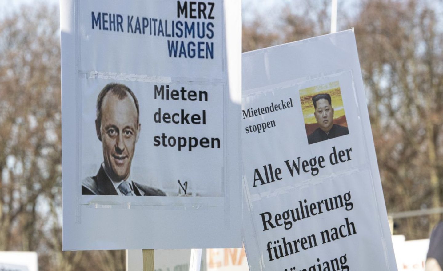 Zwei Schilder mit einem Foto von Friedrich Merz und Kim Jong Un werden auf einer Kundgebung eines Bündnisses der Berliner Bau- und Wohnungswirtschaft und von Vermietern gegen den Mietendeckel vor dem Brandenburger Tor in die Höhe gehalten