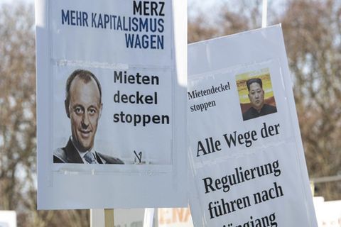 Zwei Schilder mit einem Foto von Friedrich Merz und Kim Jong Un werden auf einer Kundgebung eines Bündnisses der Berliner Bau- und Wohnungswirtschaft und von Vermietern gegen den Mietendeckel vor dem Brandenburger Tor in die Höhe gehalten
