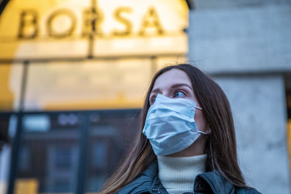 Eine Frau mit Atemmaske steht vor der Mailänder Börse