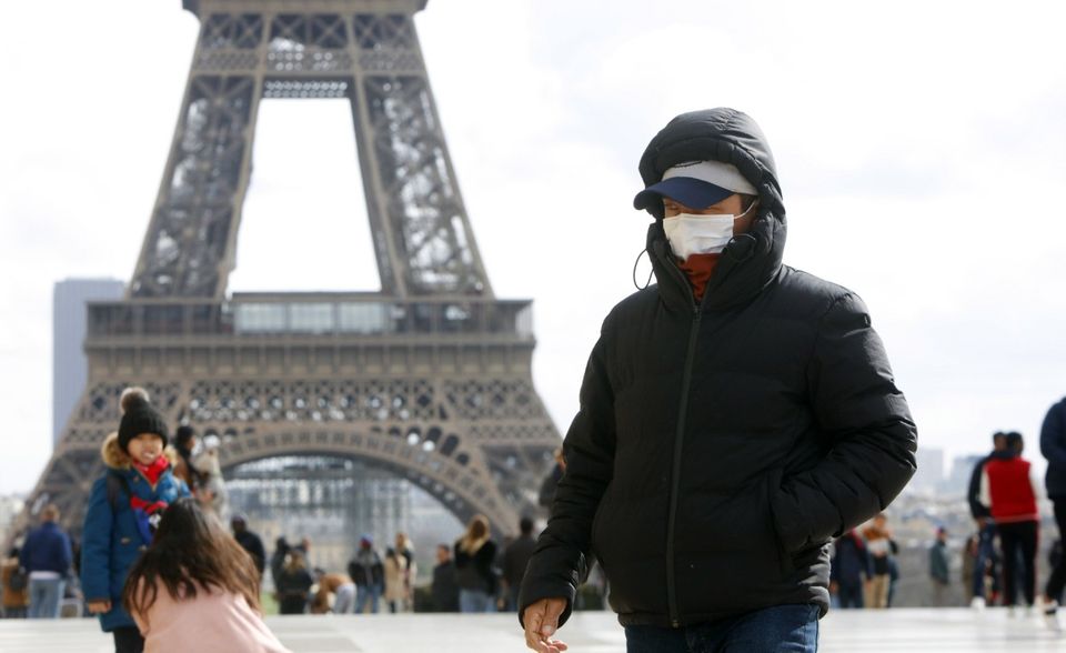 Bei 285 Menschen in Frankreich wurde der neuartige Erreger bislang nachgewiesen. Die WHO zählte vier Todesfälle. Vor dem Eiffelturm in Paris sind Menschen mit Mundschutz zu sehen.