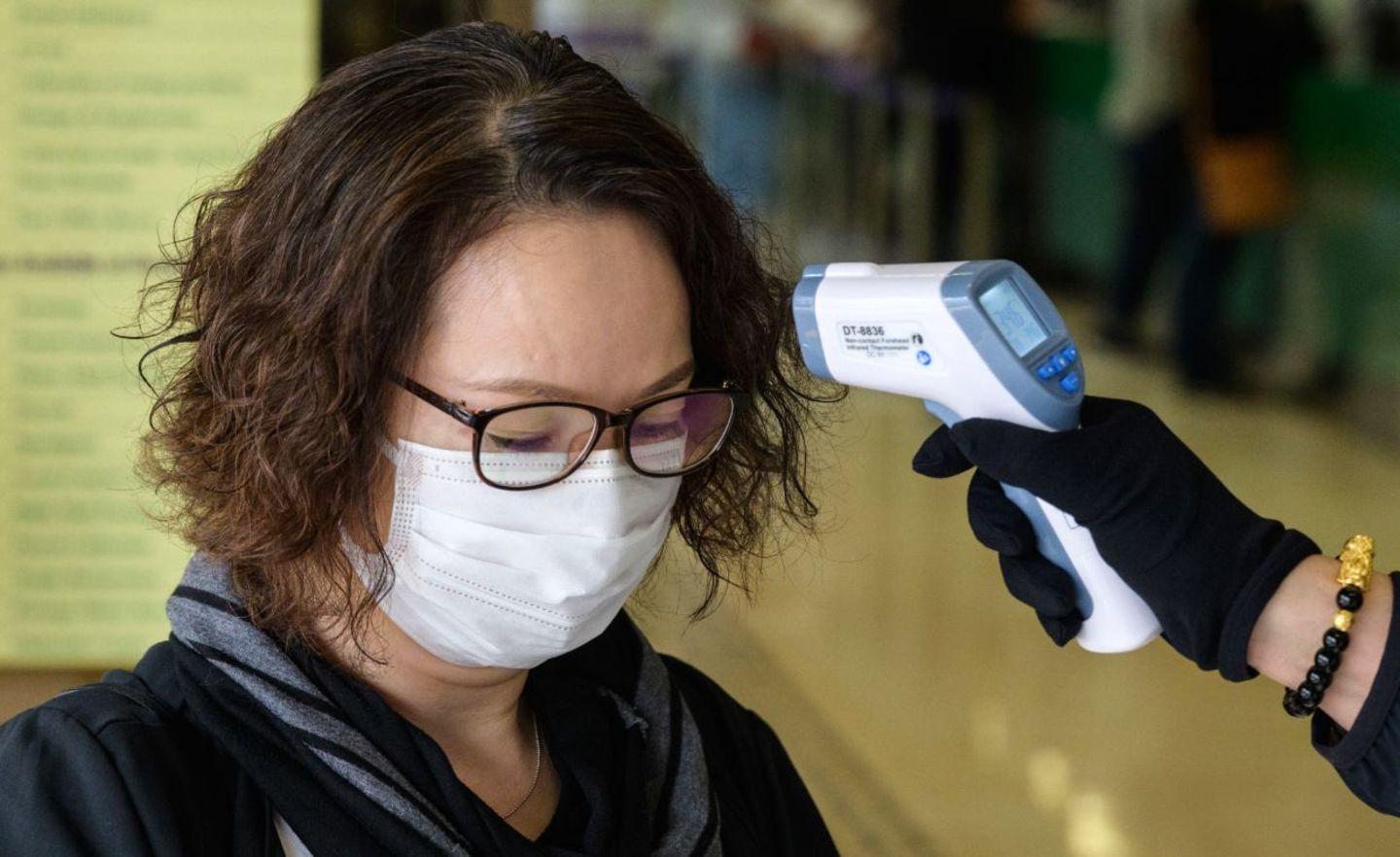 Bei einer Frau mit Gesichtsmaske wird die Temperatur gemessen. Vorher darf sie das Postamt nicht betreten