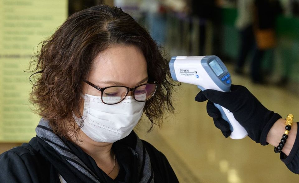 Bei einer Frau mit Gesichtsmaske wird die Temperatur gemessen. Vorher darf sie das Postamt nicht betreten