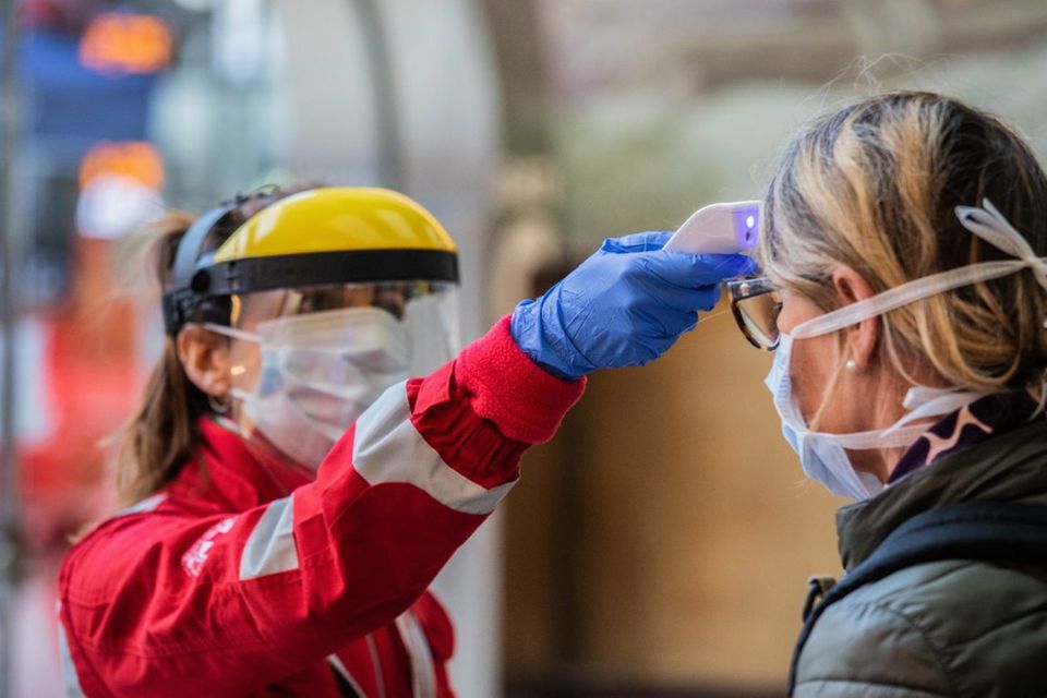 Eine Helferin misst die Körpertemperatur einer Frau am Mailänder Hauptbahnhof. Italien ist besnders schlimm von der Corona-Pandemie betroffen