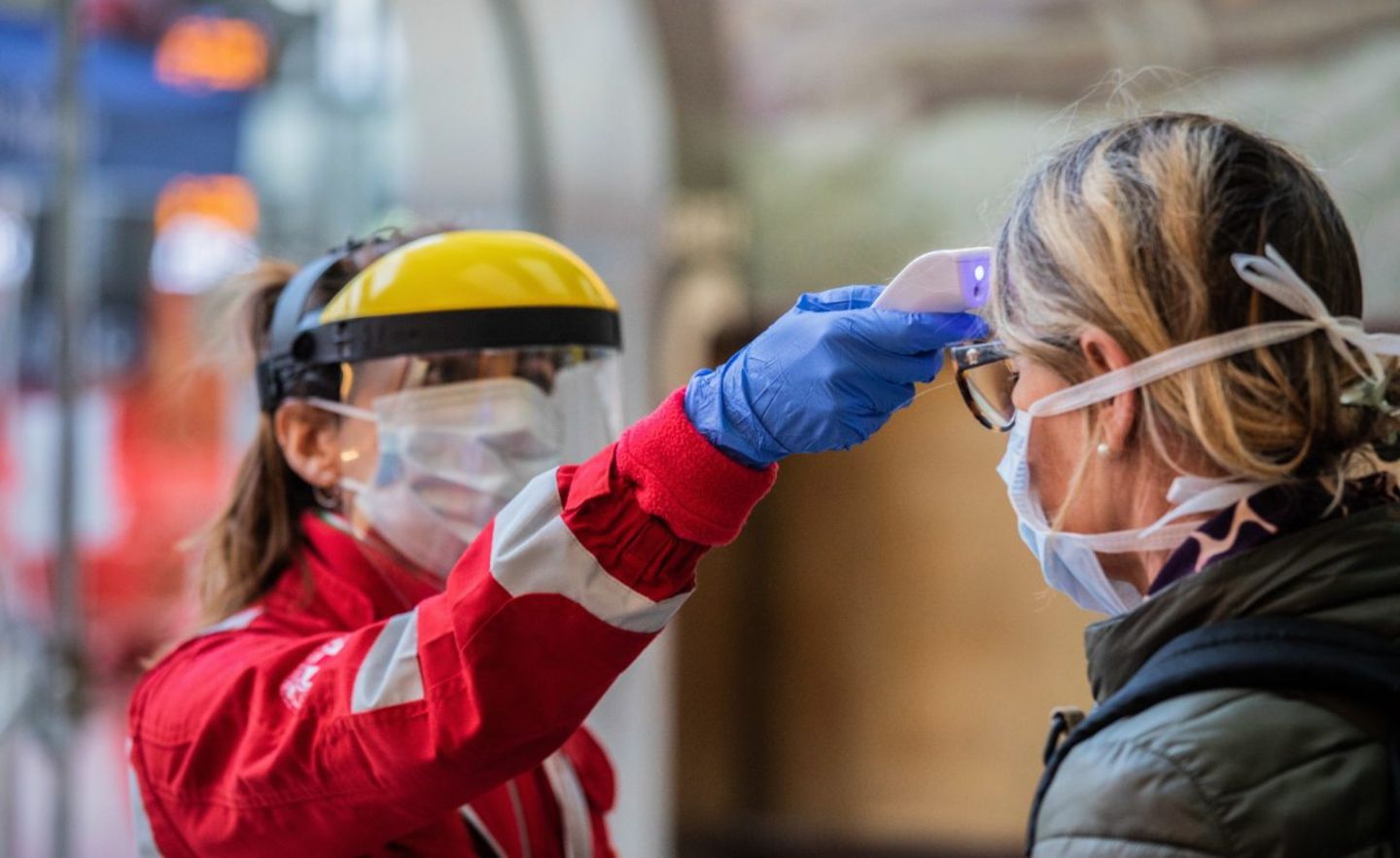Eine Helferin misst die Körpertemperatur einer Frau am Mailänder Hauptbahnhof. Italien ist besnders schlimm von der Corona-Pandemie betroffen