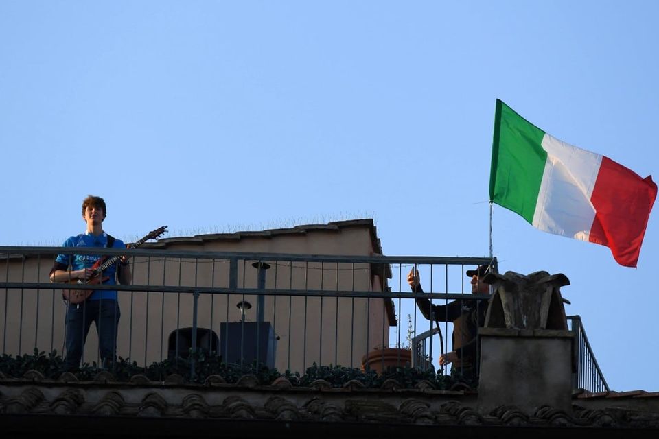 Ein Mann steht auf einem Dach und spielt Guitarre, neben ihm weht die italienische Flagge