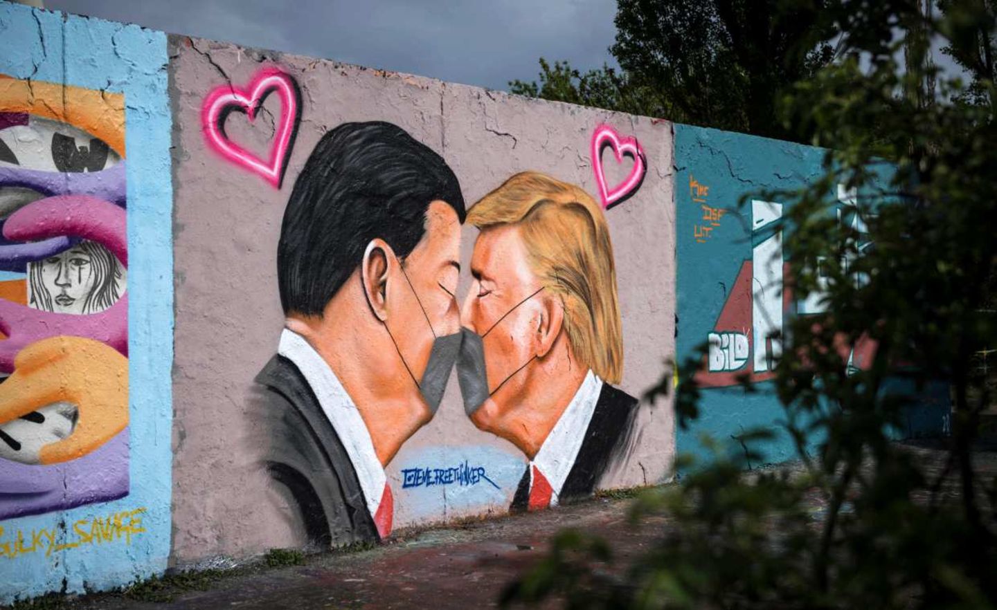 Chinas Staatschef Xi Jinping (l.) und US-Präsident Donald Trump sind auf einem Graffitto des Straßenkünstlers Eme Freethinker küssend und mit Mundschutz zu sehen