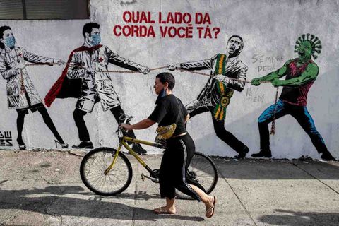 Dieses Graffito in Sao Paulo zeigt ein Tauziehen zwischen Ärzten und Brasiliens Präsident Bolsonaro, der das Coronavirus auf seiner Seite hat. „Auf welcher Seite des Seils stehst Du?“, steht auf der Wand