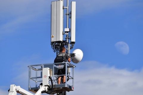 Mobilfunkmast auf einem Hausdach: Ein Mann steht auf einer Hebebühne und arbeitet an einem Antennenmast