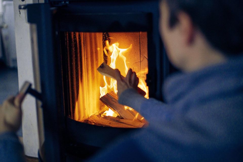 Eine Frau legt einen Holzscheit in einen Kaminofen