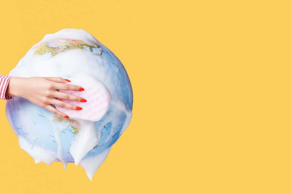Still life image of a globe being washed by a hand with a sponge to symbolise cleaning and saving the planet.