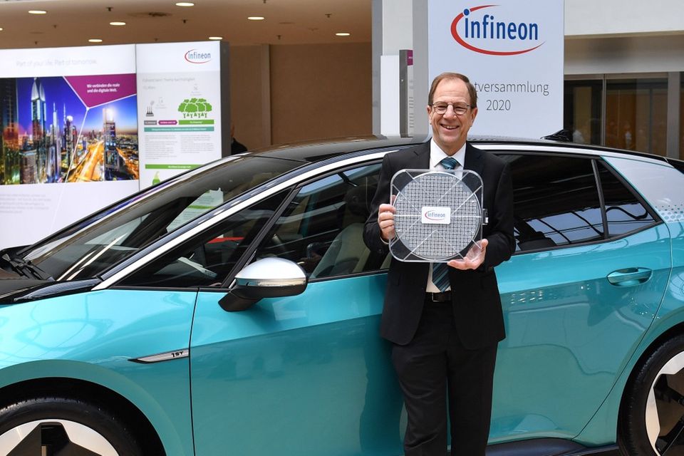 Der Vorstandsvorsitzende von Infineon, Reinhard Ploss, zeigt einen Halbleiter mit 30 Zentimeter Durchmesser vor einem VW id3 Elektroauto.
