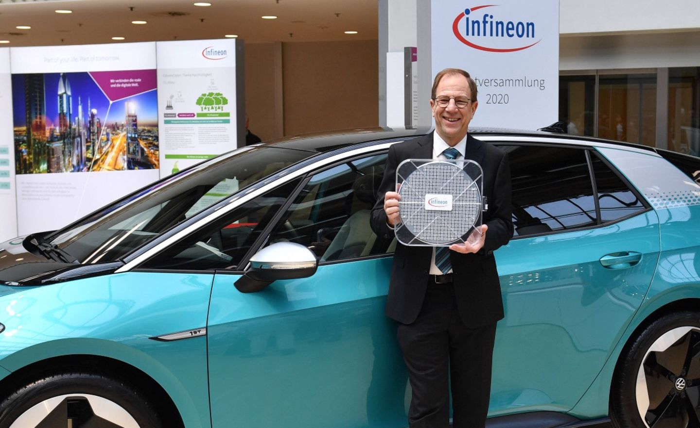 Der Vorstandsvorsitzende von Infineon, Reinhard Ploss, zeigt einen Halbleiter mit 30 Zentimeter Durchmesser vor einem VW id3 Elektroauto.