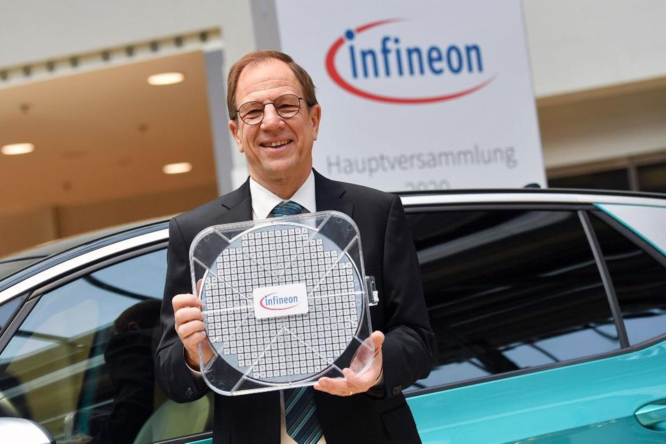 Infineon-Chef Reinhard Ploss steht mit einem Waver vor einem VW ID.3