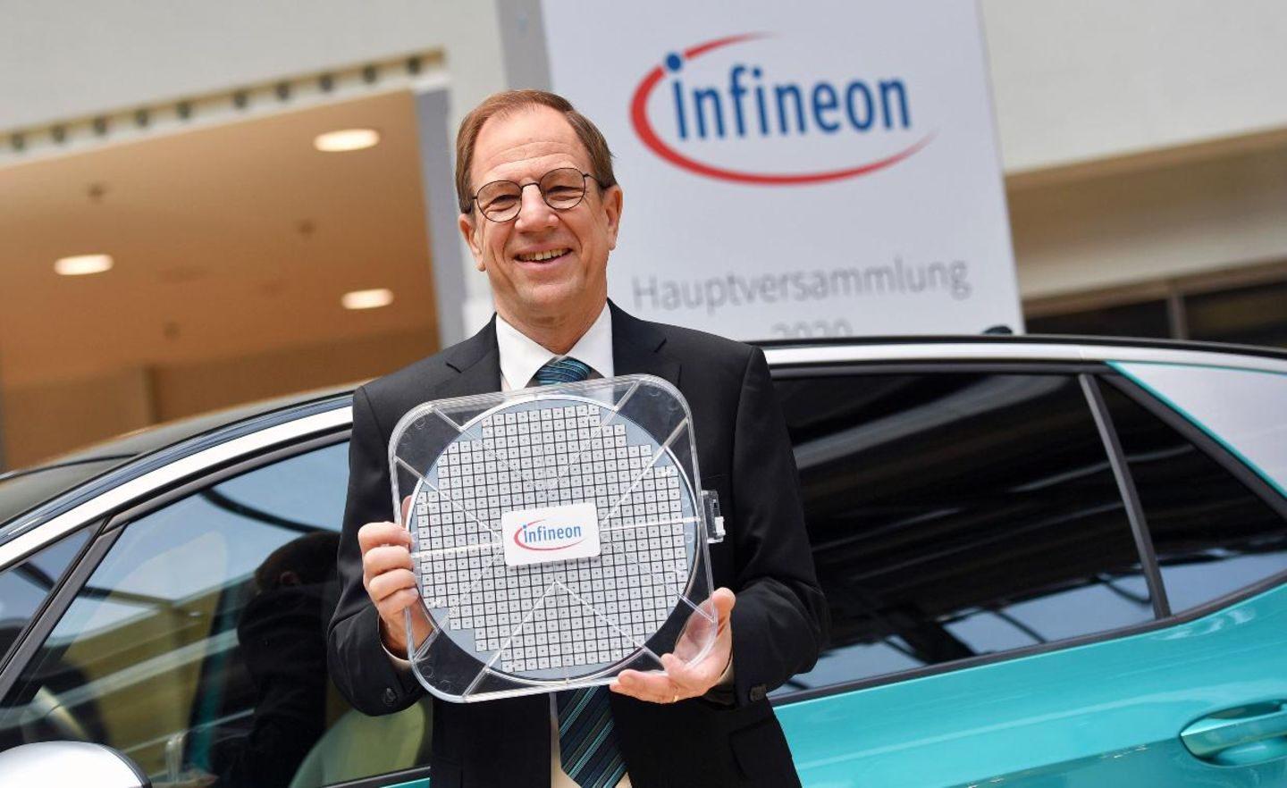 Infineon-Chef Reinhard Ploss steht mit einem Waver vor einem VW ID.3