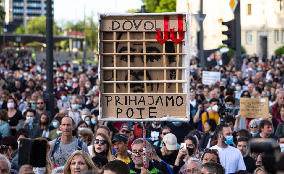 Bei einem Protest gegen die slowenische Regierung hält ein Demonstrant ein Plakat mit Jansas Gesicht hinter Gittern hoch