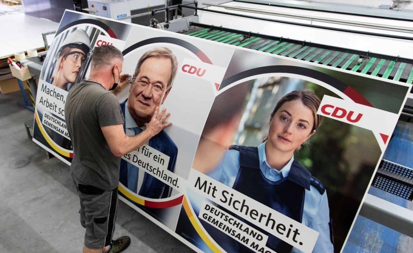 Ein Drucker kontrolliert mit einer Lupe ein Wahlplakat der CDU