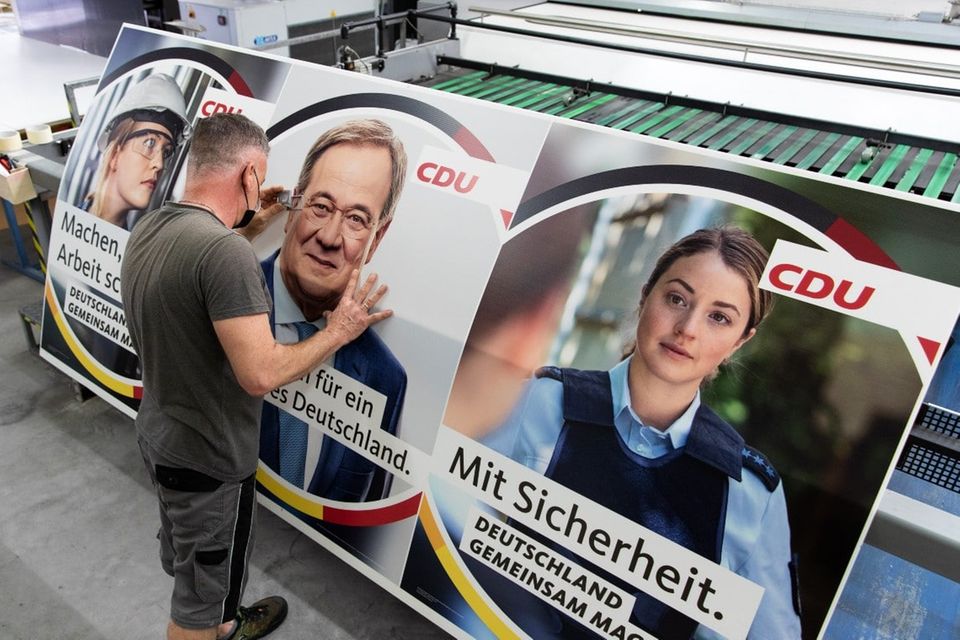 Ein Drucker kontrolliert mit einer Lupe ein Wahlplakat der CDU