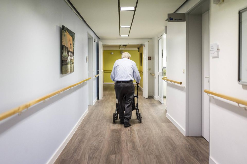 Ein alter Mann läuft mit einem Rollator im Gang einer Pflegeeinrichtung
