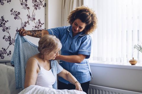 Eine Pflegerin hilft einer Seniorin beim Anziehen.