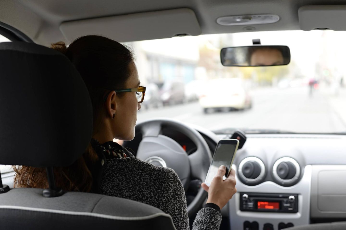 Eine Frau sitzt am Steuer eines Autos und schaut auf ihr Smartphone