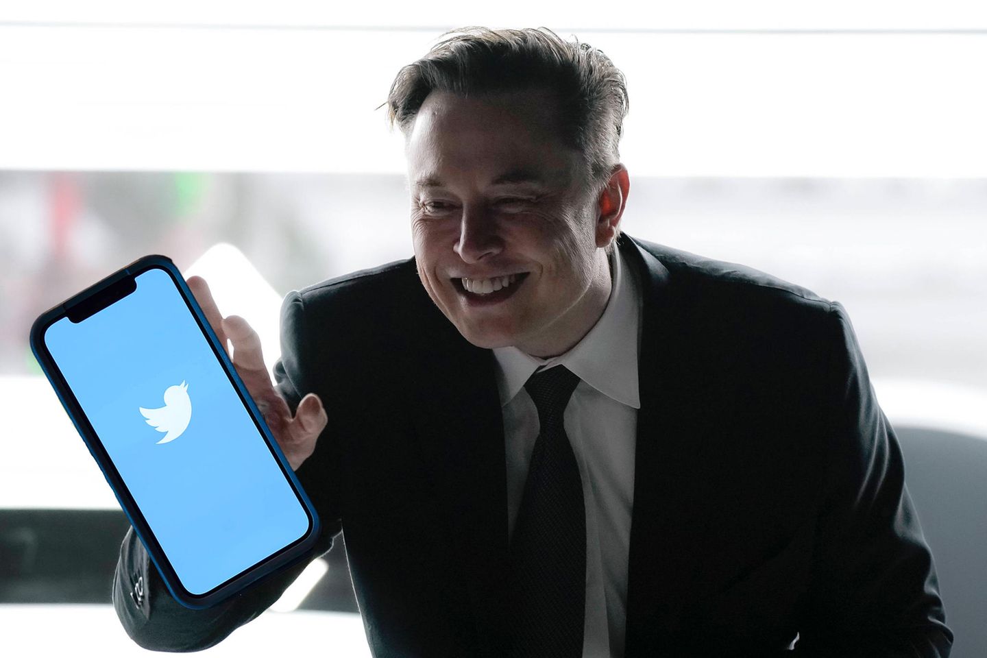 Fotomontage: Elon Musk greift nach einem Smartphone auf dem das Twitter-Logo zu sehen ist