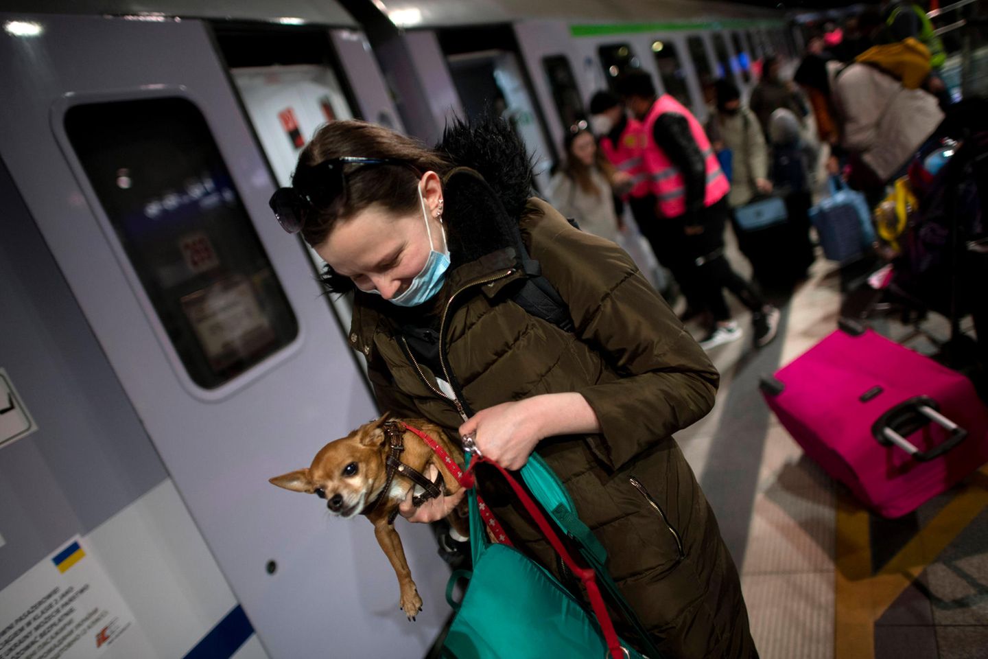 A woman with a small dog in her arms walks along a platform