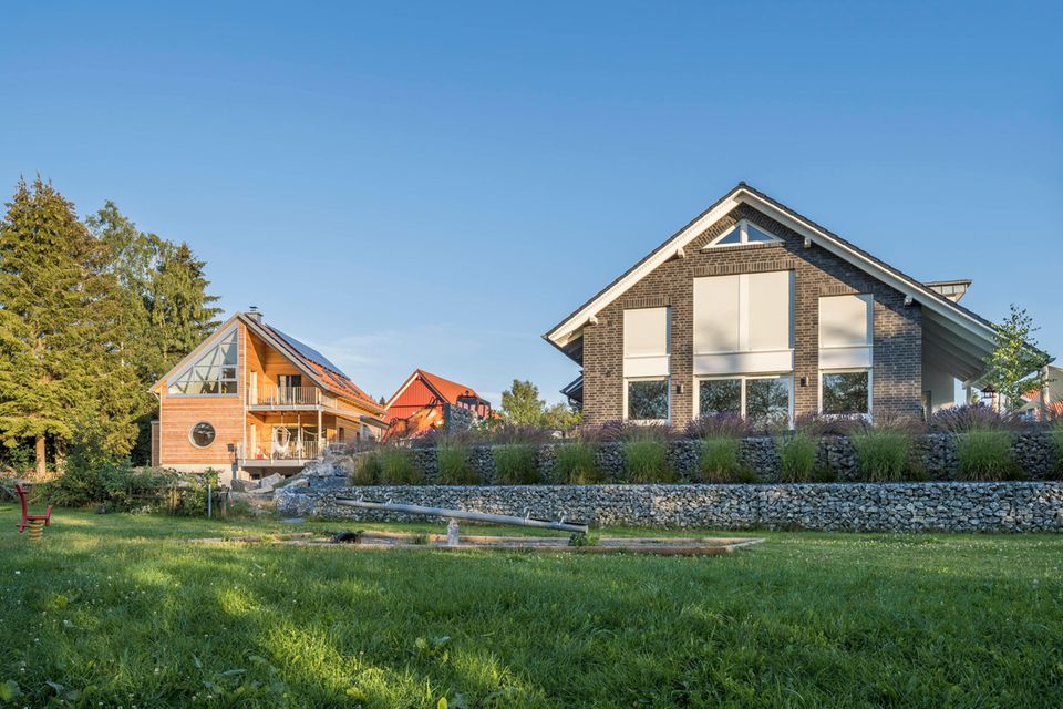 Ein Einfamilienhaus mit einer Fassade aus grauen Ziegeln und Spitzdach mit einem grünen Rasen davor