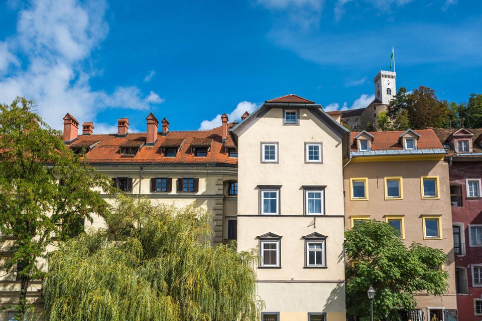 Ein Mehrfamilienhaus mit beiger Fassade und roten Dachziegeln an einem Fluss in Ljubljana