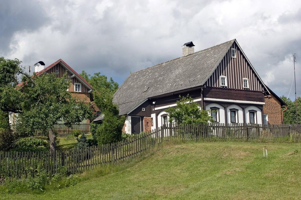 Ein Haus mit weißer und brauner Fassade und grauem Schrägdach an einem begrasten Hügel