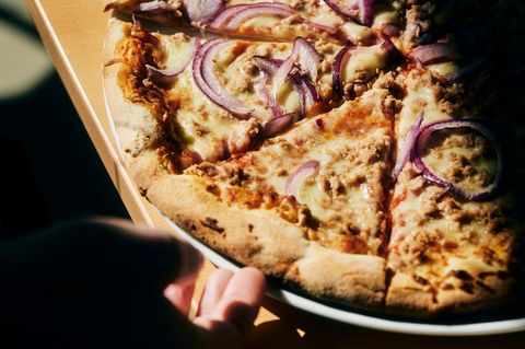 Eine Hand greift nach einem Stück Thunfisch-Pizza von Gustavo Gusto