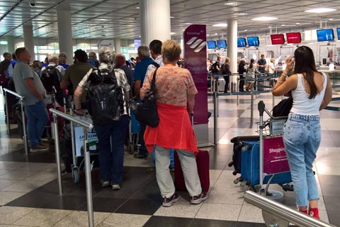 Reisende stehen am Flughafen München Schlange vor einem Check-in-Schalter
