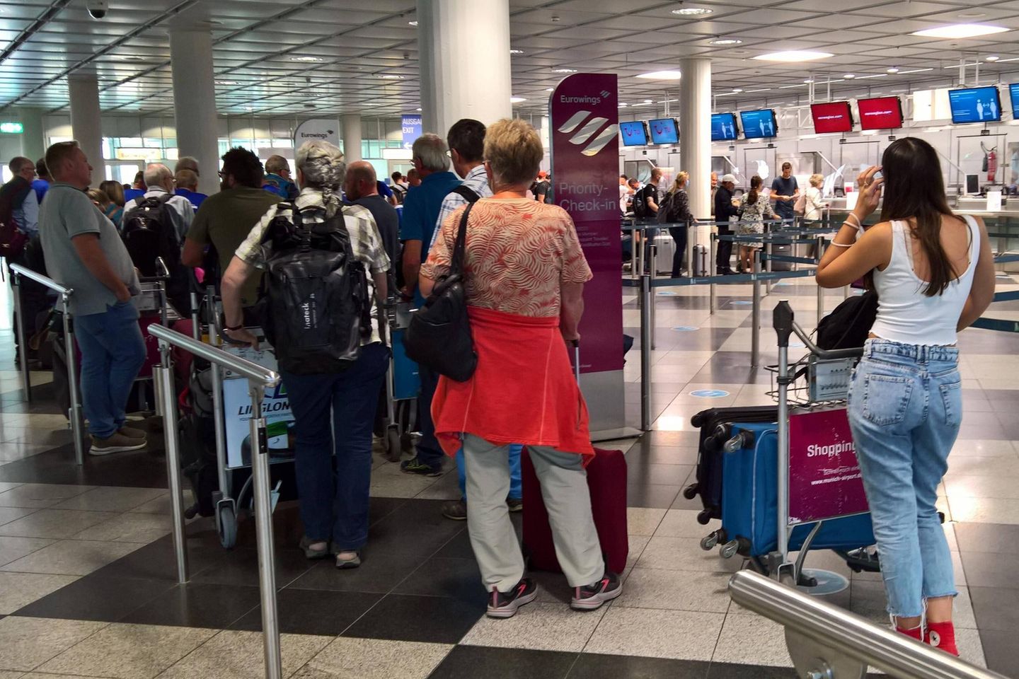 Reisende stehen am Flughafen München Schlange vor einem Check-in-Schalter