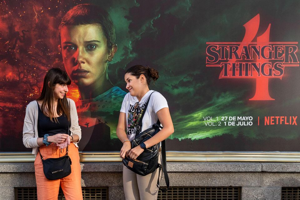 Zwei junge Frauen unterhalten sich vor einem Werbeplakat der Netflix-Serie Stranger Things