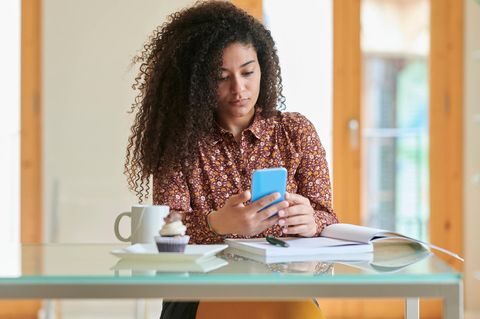 Eine junge Frau am Tisch beugt sich über ihr Handy und ihre Notizen