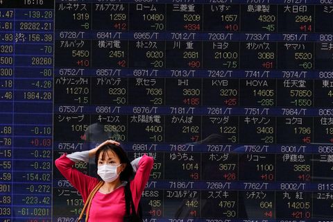 Eine Frau mit einer Maske geht an einer Börsentafel in Tokio vorbei