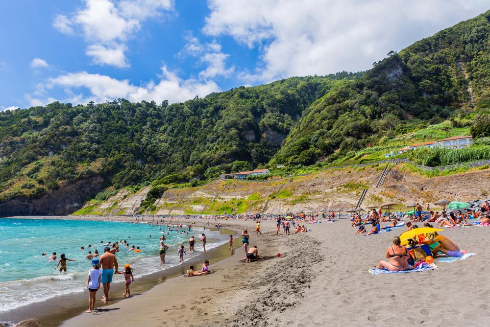 Ein Sandstrand mit Menschen und bewaldeten Bergen im Hintergrund