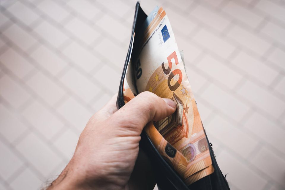 Ein Mann hält ein Portmonnaie mit Bargeld in der Hand