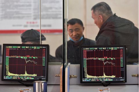 Der Index der Börse von Schanghai wird auf Monitoren angezeigt, während sich im Hintergrund drei Männer unterhalten